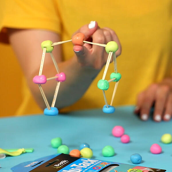 Hand holding a colourful Blu Tack and toothpick structure for the Finger Balance Challenge game.