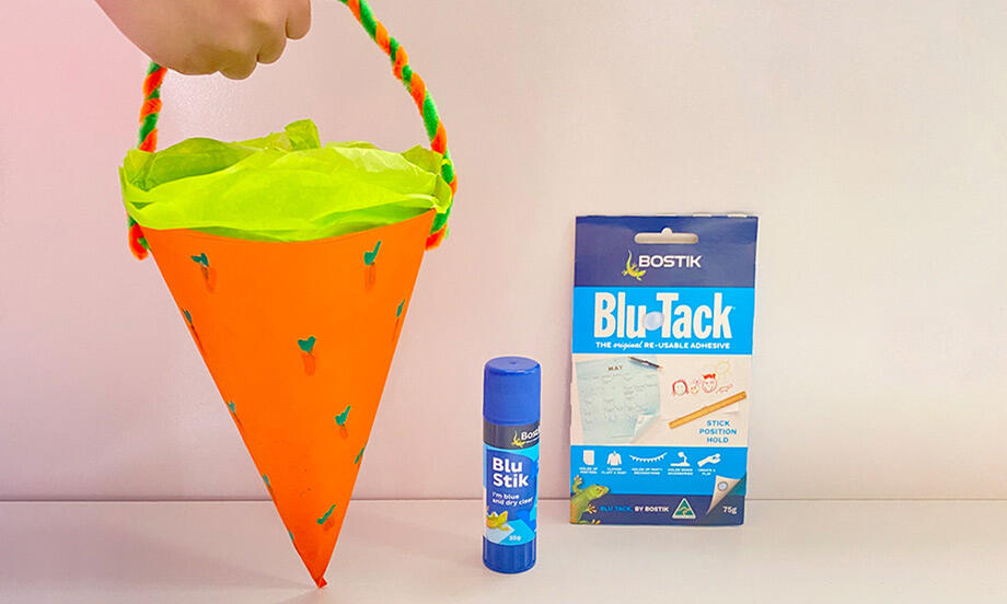 Bright and fun Easter carrot-shaped basket made from orange paper with green tissue lining, perfect for holding treats.