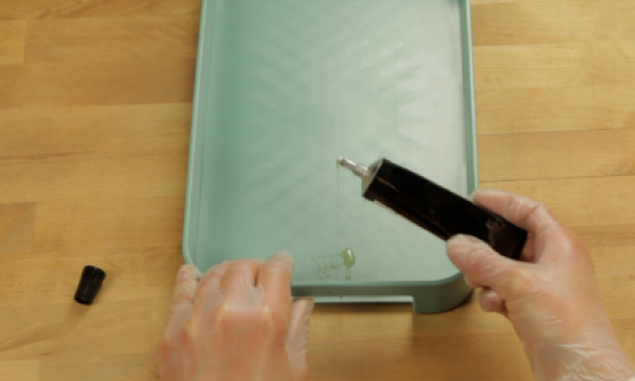 Applying Bostik adhesive remover to a small glue spot on a green plastic tray.