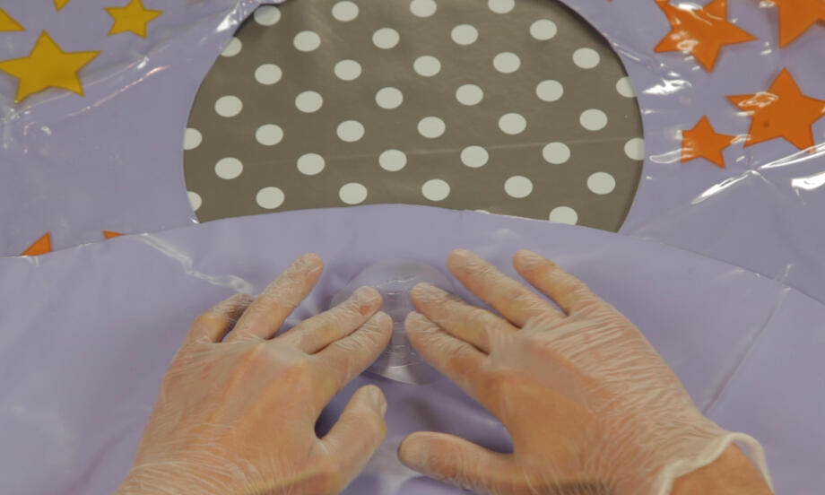 Mâini cu mănuși presează zona suspectă a colacului gonflabil pentru a localiza perforația, pregătind suprafața flexibilă pentru reparare cu adeziv.