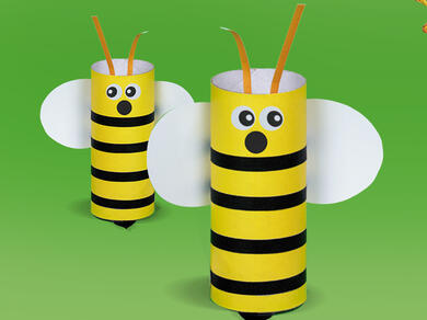 A fun paper bee craft made with a toilet roll, glue stick and scissors on a green background.