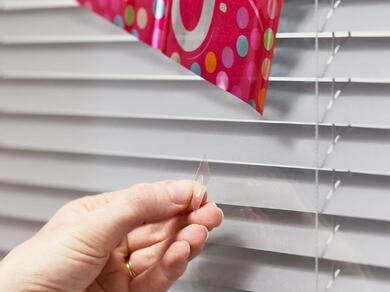 Hands attaching a colourful birthday banner to a surface using Glu Dots.