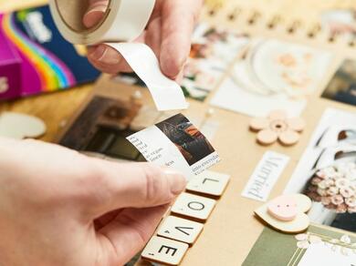 Hands peeling a strip of Glu Dots to attach a photo in a scrapbook layout.
