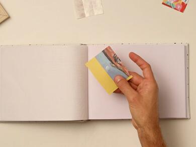 A hand holding a small printed photo with a yellow paper backing for scrapbook placement.
