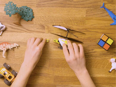 Person applying Bostik Hard Plastics adhesive to repair the tail of a broken toy helicopter.