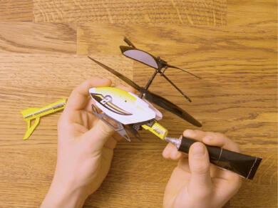Person applying Bostik Hard Plastics adhesive to repair the tail of a broken toy helicopter.