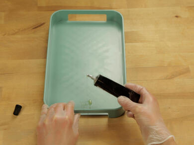 Applying Bostik adhesive remover to a small glue spot on a green plastic tray.