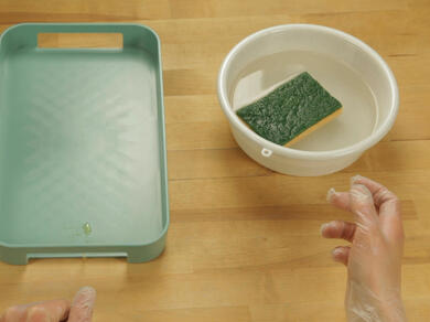 Used sponge resting in a bowl of water next to a clean plastic tray.