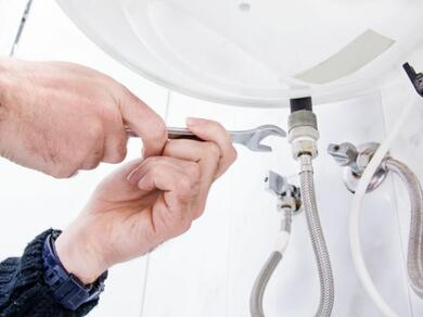 A person uses a spanner to tighten plumbing under a sink to stop a leak.