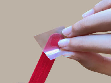 Fingers peeling a red extra strong Bostik Glu Dot from its clear backing sheet, ready for use in a DIY project.