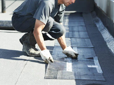 Worker installing waterproof membrane strips on a flat rooftop for weather protection