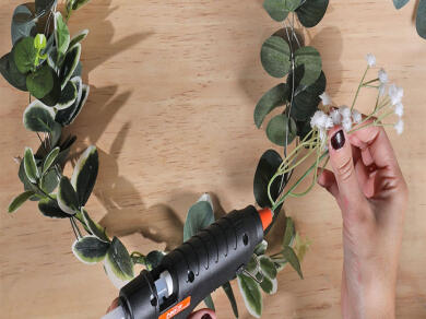A handmade DIY wreath decorated with lush green leaves and delicate white flowers displayed on a wooden surface.