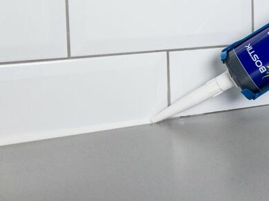 Close-up of Bostik sealant being applied to white bathroom tiles for a water-tight seal.