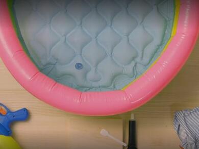 A repaired hole visible inside a pink inflatable paddling pool, with glue and a cloth nearby.