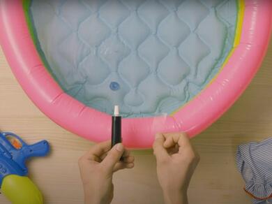 Hands applying a clear plastic patch to the outer wall of a paddling pool using Bostik glue.