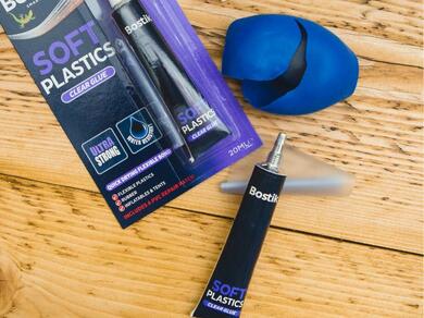 A tube of Bostik Soft Plastics Clear Glue next to its packaging and a torn plastic ball, ready for repair.