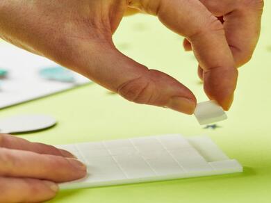 Hand picking up a medium-sized Bostik Foam Pad from the backing sheet.