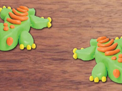 A playful Blu Tack craft scene featuring geckos, a blue pond, and colourful plants made from modelling pieces.