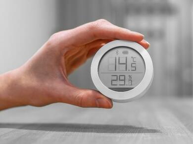 A hand holding a digital hygrometer showing indoor humidity level.