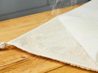 Spray glue being applied to the back of a rug for secure bonding.
