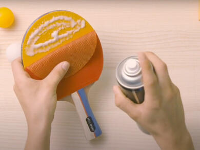 Spray glue being sprayed onto a table tennis paddle for strong rubber adhesion.