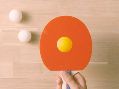 Ping pong paddle with a yellow ball in the centre, ready for playing a game of table tennis.
