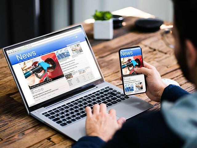 Person checks the same news article on a laptop while holding a smartphone at a desk; hero banner for News, Events & Blogs