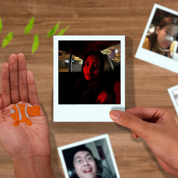 A person holds an instant photo while preparing a cute fish-shaped Blu Tack design to display it