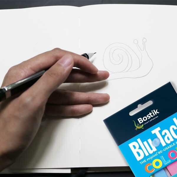 Hand drawing a snail in a notebook next to a finished Blu Tack snail sculpture for inspiration.