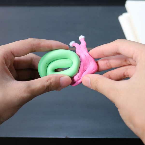 Hands pressing together pink and green Blu Tack to form the snail’s body and shell.