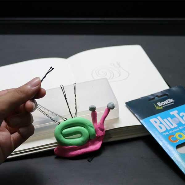 Hands shaping pink and green Blu Tack into a snail body, starting the mini sculpture project.