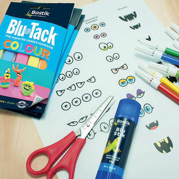 Close-up of colourful monster eyes and mouths cut out from paper, with red scissors and a Bostik Blu Stik glue stick on a wooden surface.