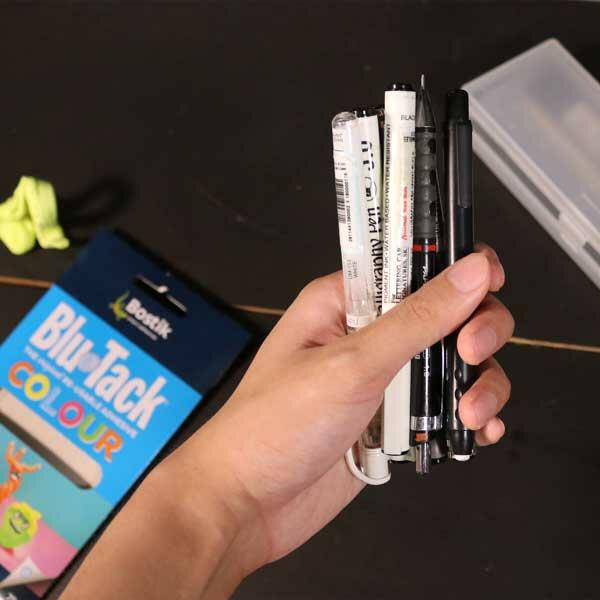 A hand holding several pens bundled together, ready to start the Blu Tack activity.