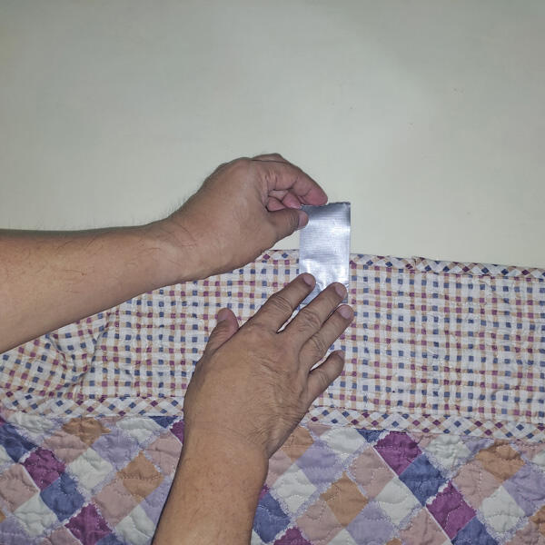 Hands pressing patterned fabric with adhesive tape against the wall.