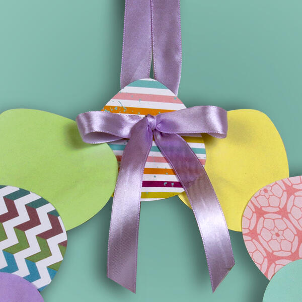 Patterned paper egg shapes are glued around the paper plate base using Bostik Glue Stick, forming a festive ring.