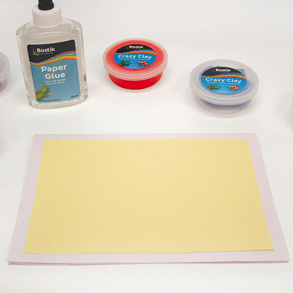A blank yellow card is placed on a table alongside tubs of Bostik Crazy Clay and a bottle of Bostik Paper Glue, ready for crafting.