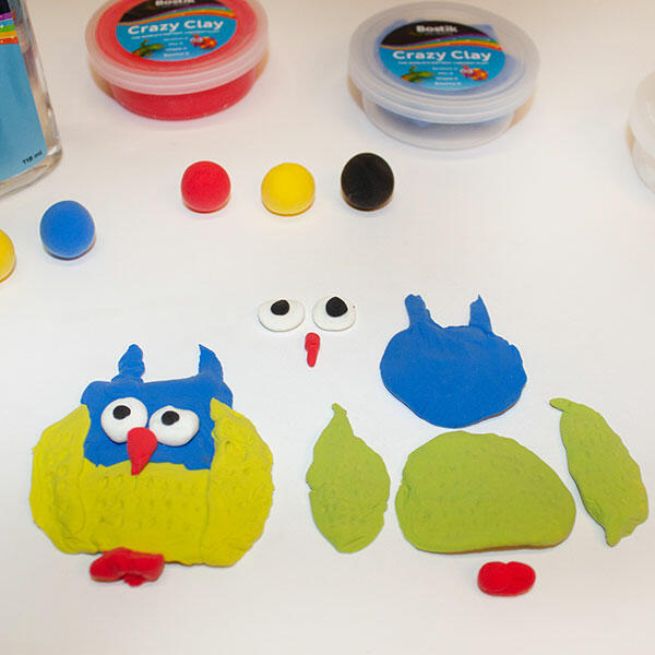 Owl body parts are shaped from blue, green, and yellow clay, with one owl already assembled and the other in progress.