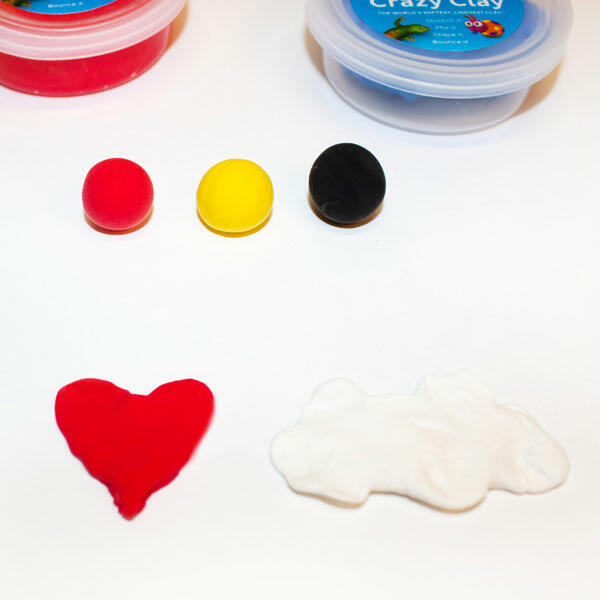 A red heart and white cloud made of clay are prepared alongside three small balls of clay: red, yellow, and black.