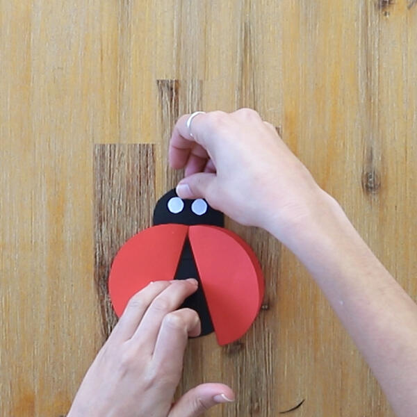 Two hands press white paper circles onto the head to create the ladybug’s eyes.