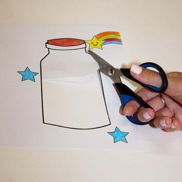 A pair of hands using scissors to carefully cut around the top jar design with colourful stars and a rainbow.
