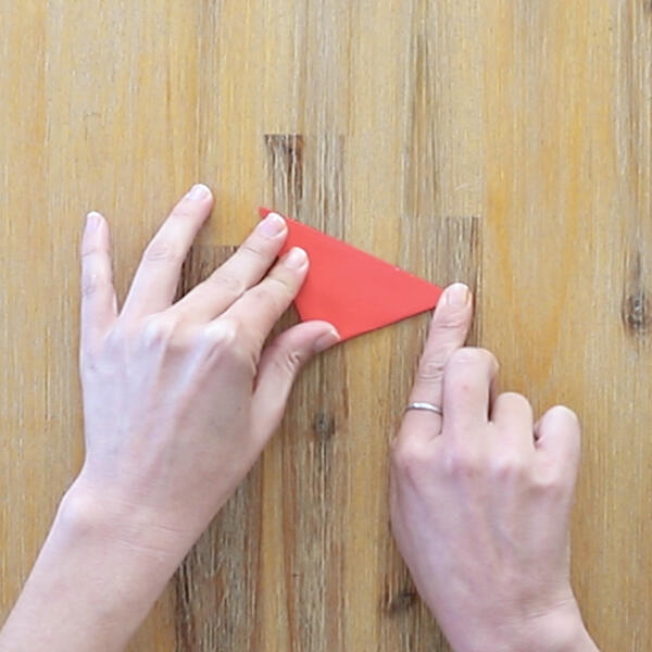 Folding the red square into a triangle in preparation for petal shaping.