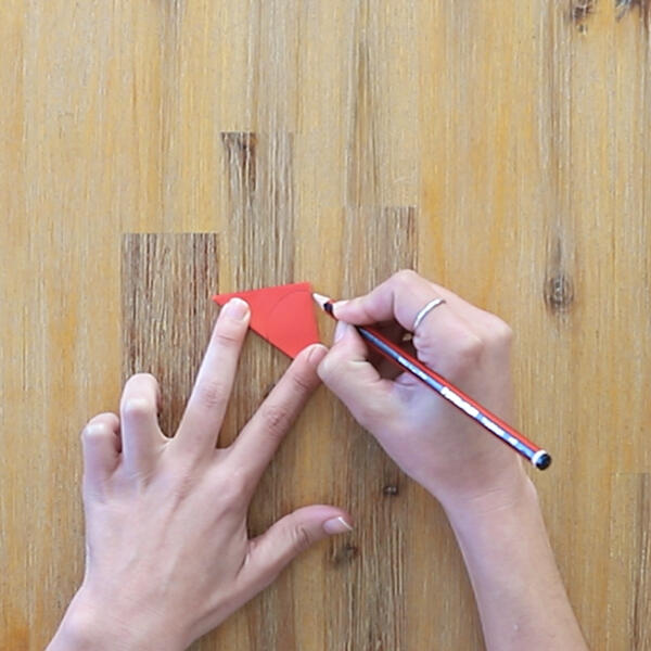 Drawing a petal shape on the folded triangle using a pencil.