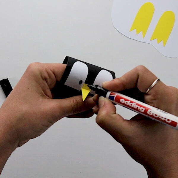 Drawing black pupils onto the penguin's eyes using a marker for a playful look.