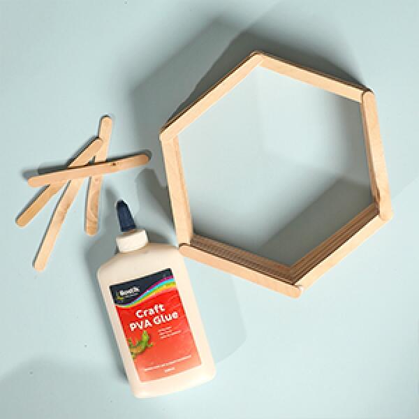 Applying glue to popsicle sticks laid on the hexagon template to start building the shelf structure.