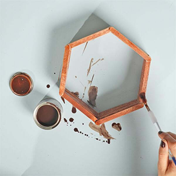 Stacking and gluing multiple layers of popsicle sticks on top of each other to create a thicker hexagon frame.