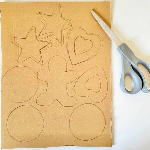 Cardboard sheet with traced outlines of cookies and shapes, ready to be cut out with scissors.