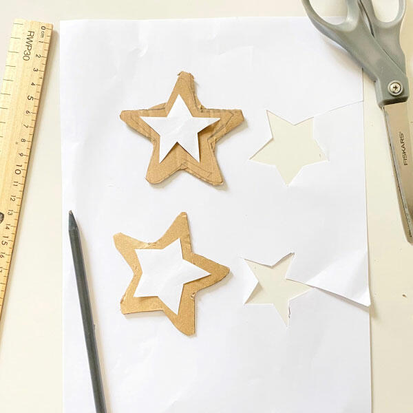 Cut-out star shapes from cardboard with white paper templates placed on top, pencil and scissors nearby.