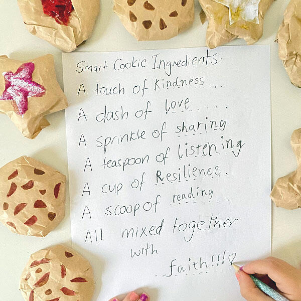 A handwritten “Smart Cookie Ingredients” list surrounded by decorated cookies, with a child writing the last word.