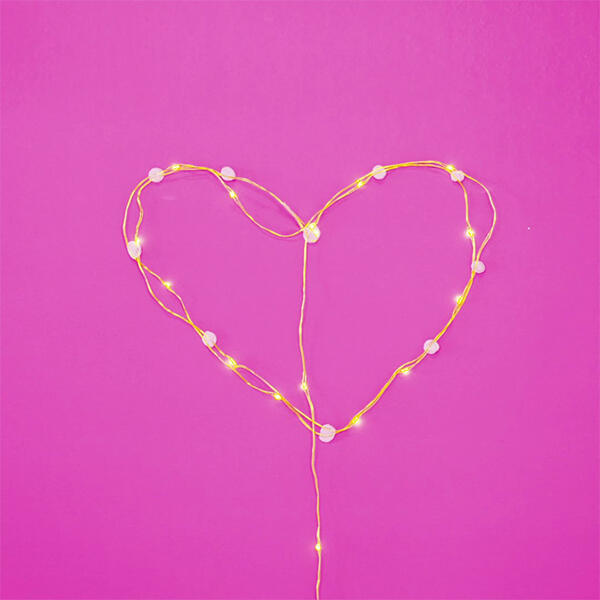 String lights shaped into a heart against a vibrant pink background, secured with Blu Tack.