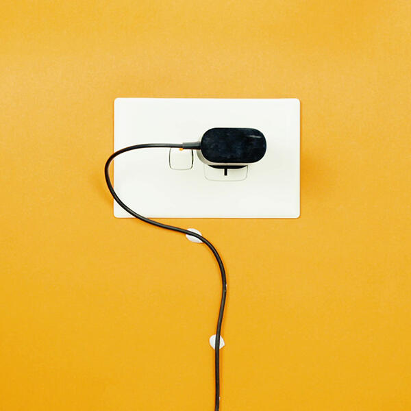 Power cable neatly held in place with Blu Tack against an orange wall near a wall socket.